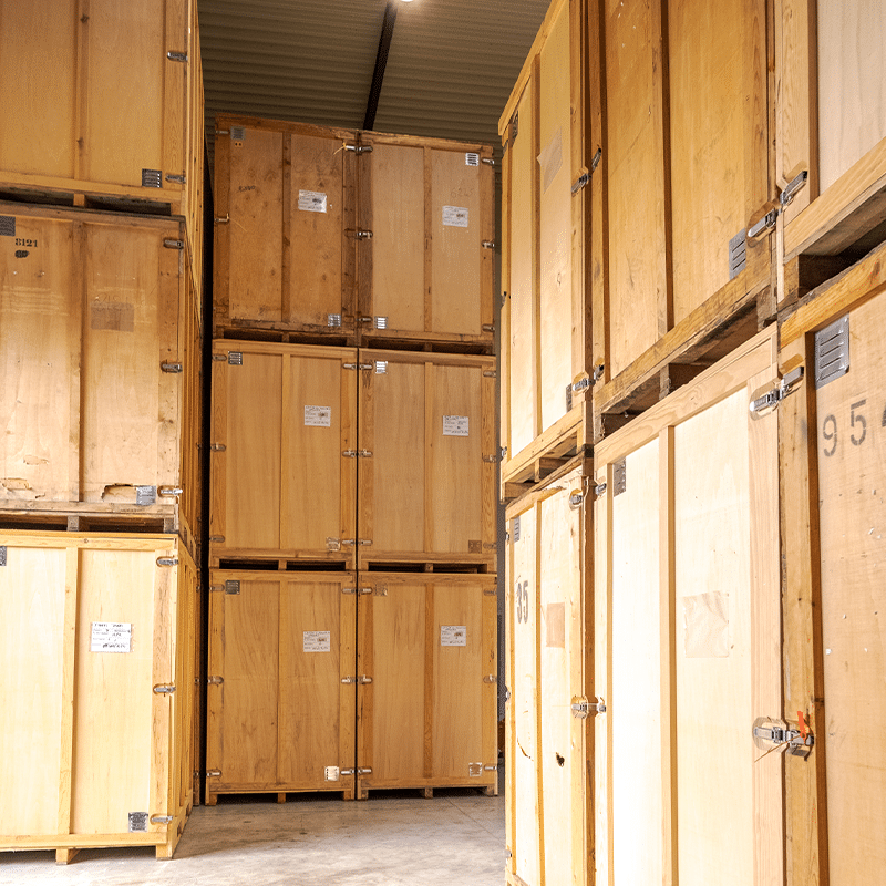 Un agent Proconcept de dos en veste rouge marchant dans l'allée d'un entrepôt de garde-meubles entouré de box de stockage en bois.