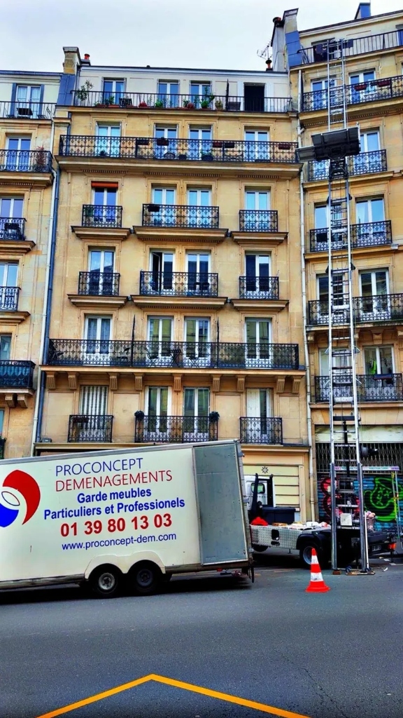 Remorque capitonnée Proconcept stationnée devant un immeuble haussmannien parisien avec un monte-meuble déployé jusqu'aux balcons des derniers étages.