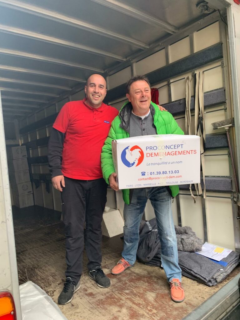 Deux déménageurs professionnels souriants à l'arrière d'un camion de déménagement, tenant un carton d'emballage Pro Concept Déménagements.