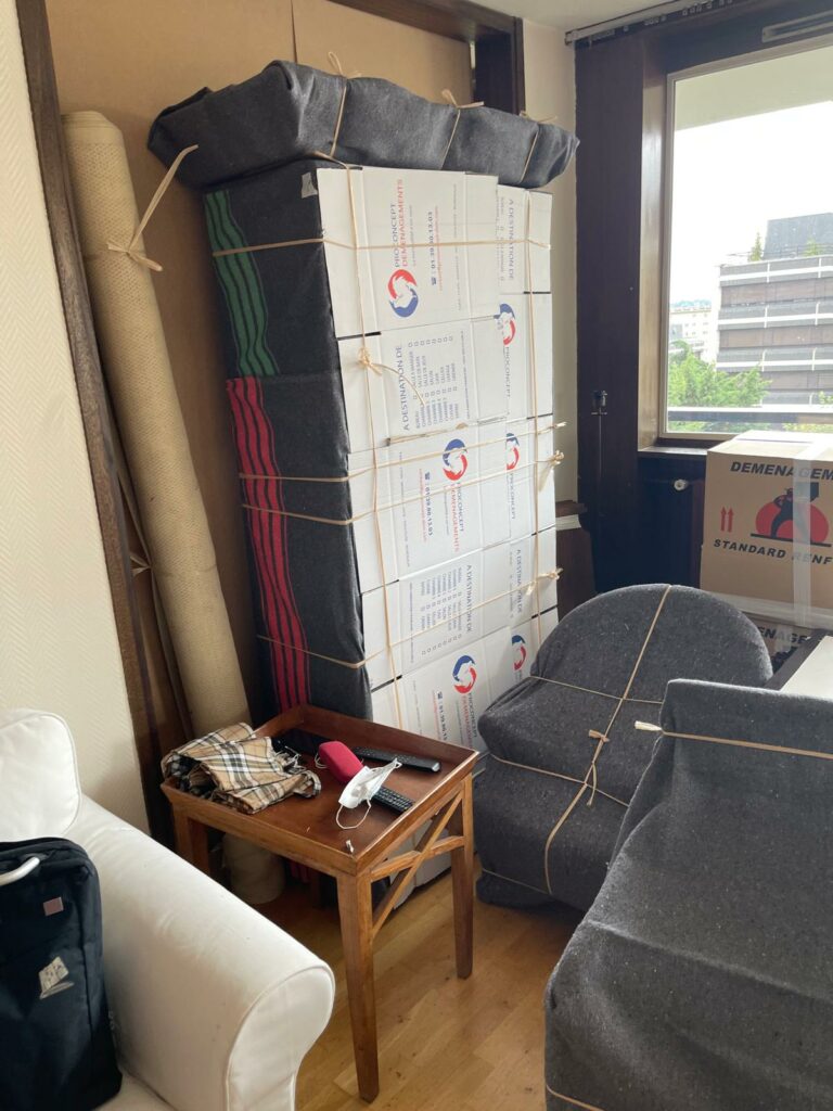 Pile de cartons d'emballage Pro Concept Déménagements et meubles protégés sous couvertures dans une pièce avant le transport.