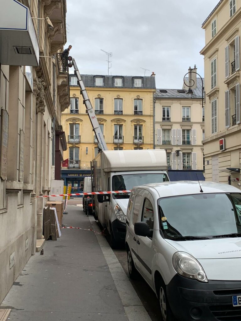 Monte-meuble télescopique déployé sur le balcon d'un immeuble parisien sécurisé par un ruban de signalisation pour un déménagement.